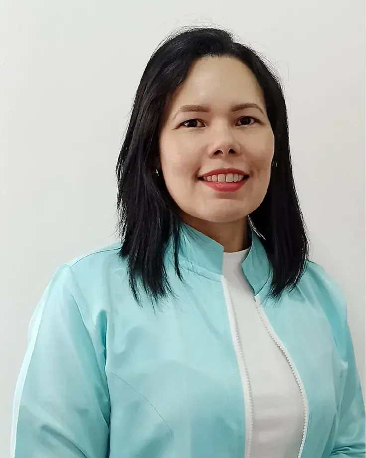 La Dra. Nuramí Rojas sonriendo, con filipina color aguamarina sobre camisa blanca, frente a una pared clara